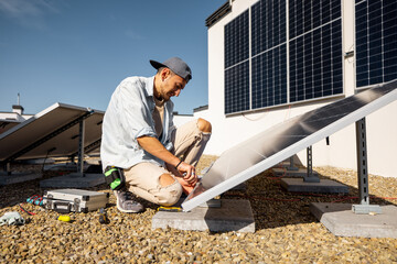 Man installing solar panels on the roof of his house, screwing cell on flat rooftop for self consumption. Renewable energy and sustainability concept