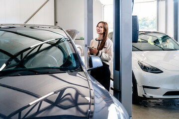 Using smartphone while waiting. Young business woman on the electric cars waiting at auto service...