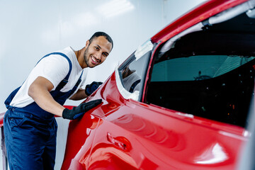 Portrait of happy arabian man admires his work checking a red car after painting. Automotive paint services, quality auto body shop concept.