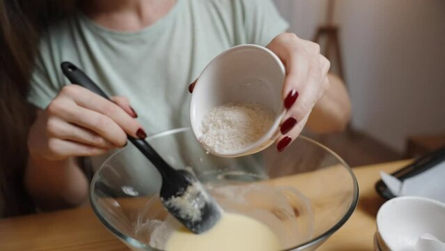A young woman adds coconut flakes to the dough as she prepares cookie batter. In slow motion.