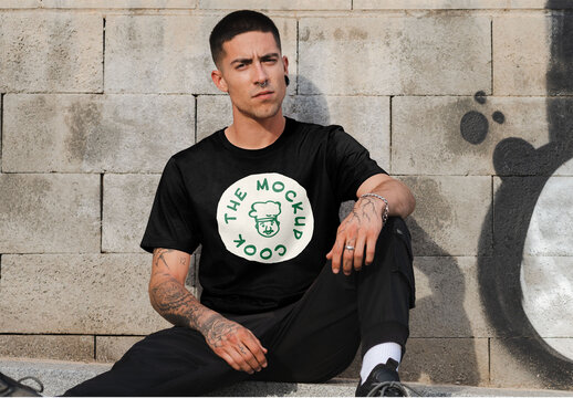 Mockup of man wearing t-shirt with customizable color and design sitting by wall