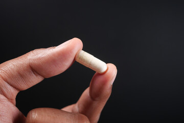 Close up of man hand holding capsule against black background 