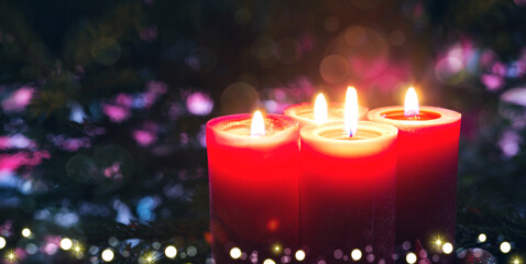 Four burning red Advent candles on fir tree background.