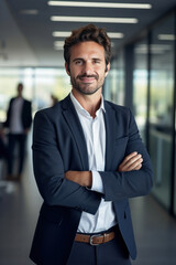 Fototapeta premium A smiling businessman standing in front of a camera with his arms crossed in a modern office.