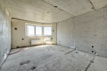 Empty living room without renovation, no repair in a new apartment building. Living room with concrete walls, floor and ceiling, no plaster