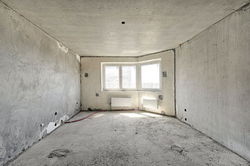 Empty living room without renovation, no repair in a new apartment building. Living room with concrete walls, floor and ceiling, no plaster