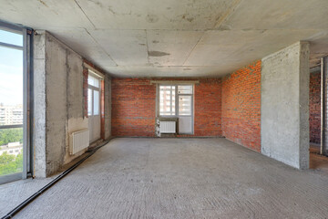 Empty living room without renovation, no repair in a new apartment building. Living room with concrete and red brick walls, concrete ceiling and floor, no plaster
