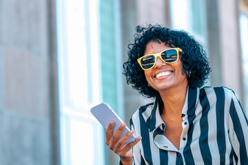 woman with headphones and mobile phone smiling with yellow sunglasses