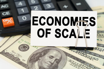 On the dollars there is a calculator and a business card with the inscription - ECONOMIES OF SCALE