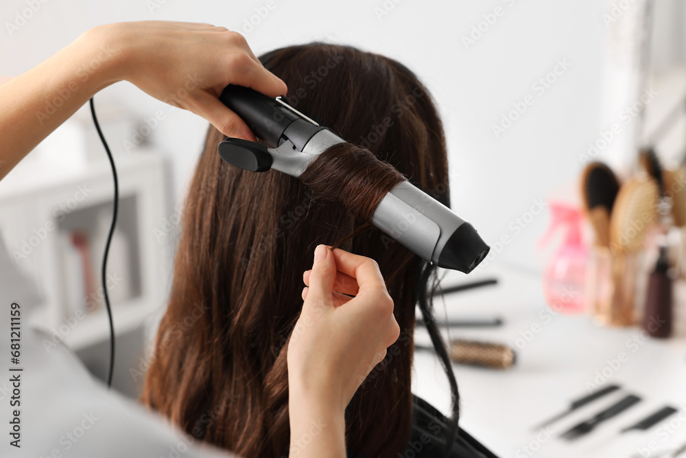 Wall mural Hairdresser working with client using curling hair iron in salon, closeup