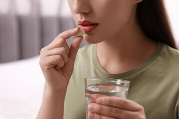 Woman with glass of water taking antidepressant pill indoors, closeup