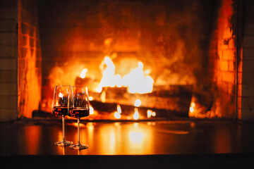 Open fire with real flames, firewood burning in fireplace with two glasses of red wine