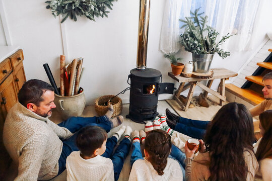 Cropped Photo Of Big Family Wearing Warm Woolen Socks Resting By Fireplace Together In Winter Time. Mother, Father And Children Lying On Floor Warming Feet Near Potbelly Stove In Country House