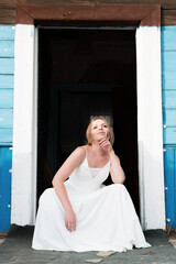 Happy young bride is sitting on the threshold of an old house.
