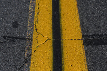 Closeup of repainted double yellow line on pavement with shrinkage cracks 