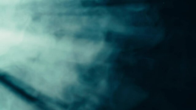 Abstract background of chaotically blending puffs of blue smoke on a black background. Realistic fog in blue neon light close up. Texture and abstract art. Copy space.