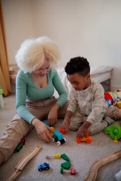 Young mother with albinism playing with son sitting on floor