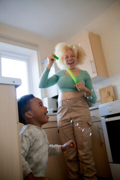 Happy young woman with albinism blowing bubbles for son in kitchen