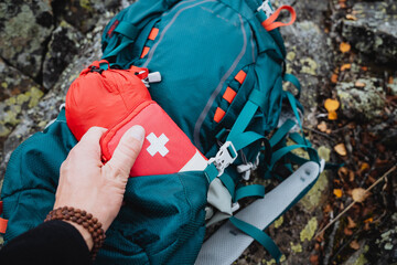 A tourist takes out a red first aid kit, a first aid kit, and camping equipment from a backpack...