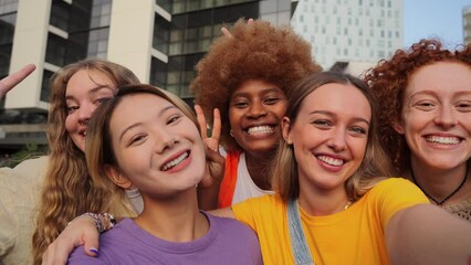 Group of young feminine women taking a selfie portrait, smiling looking at camera. Teenage girls laughing and waving hands on a stream live. Multiracial excited females having fun staring front. High