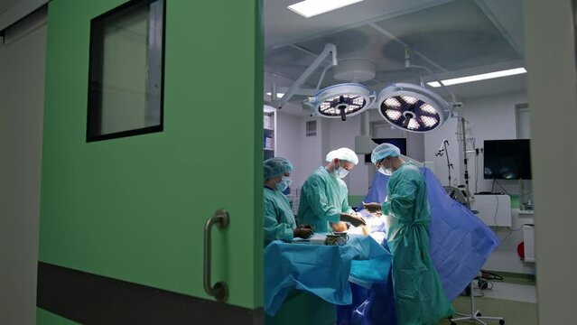 Entering The Modern Surgical Room Through The Wide Sliding Door. Two Doctors Perform Trauma Surgery On The Foot.