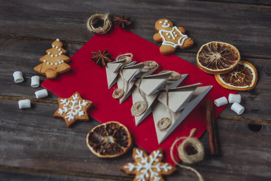 Concept of New Year or Christmas craft. Handmade card made from natural recyclable materials, paper fir tree with anise star on top. Dry citrus, gingerbread cookies, wooden background