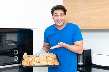 Happy guy holding a baking sheet with ready-made buns, which he just took out of the oven