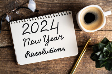 2024 New year resolutions on desk. 2024 goals list with notebook, coffee cup, plant on wooden background. Resolutions, plan, goals, action, strategy, success concept. New Year 2024 resolutions.