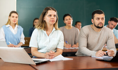 Group of adult students sitting at tables in classroom and studying.
