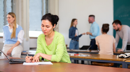 Asian woman university student sitting at table in classroom and writing.