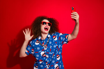 Photo of funky cool lady dressed ugly santa claus print xmas shirt recording video vlog apple samsung iphone isolated red color background