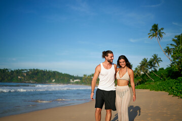 Couple walks holding hands on tropical beach, man and woman enjoy romantic stroll by sea, clear...