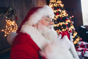 Photo of funky dreamy santa claus wear red costume spectacles closed eyes enjoying tasty hot milk indoors new year north pole office