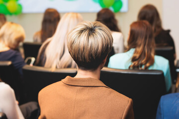 Female participants audience at the symposyum meeting, attendees in conference room hall listens to lecturer, group of women on a congress together listen to speaker on a stage at master-class