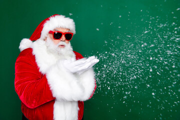 Photo portrait of mature pensioner man blow snowy weather wind dressed stylish santa claus costume coat isolated on green color background