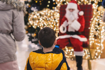 Kids waiting to meet and see Santa Claus, children asking Santa Claus for a gift on Christmas fair market in a shopping mall trade center, boys and girls visit Santa and receive gifts and presents