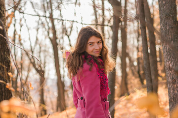 Cheerful young woman with pink scarf relaxing at park with yellow trees in background copy space. Smiling beautiful girl enjoying warm sunny weather in autumn season. Happy pretty natural woman