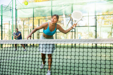 Attractive woman padel tennis player training on court. Young woman using racket to hit ball.
