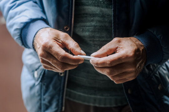 An elderly pensioner man is struggling with addiction, the desire to smoke, holding a cigarette in his hands. Medicine concept. Photography, portrait.