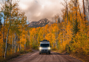 Campervan driving wild forest road with headlights on. Epic Autumn Fall foliage landscape with Mountain and blue sky in Kebler Pass Colorado