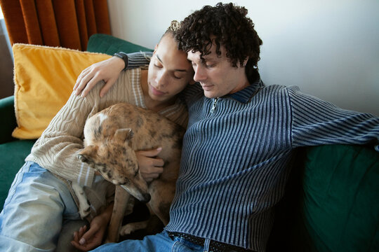Two young multiracial men sitting on couch with their dog