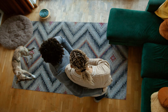 Two young multiracial guys hugging in living room looking out window photographed from above