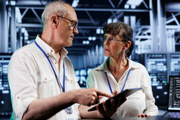 Licensed admins updating server racks, writing intricate binary code scripts on tablet and laptop. Certified engineers using programming to fortify cybersecurity in high tech establishment