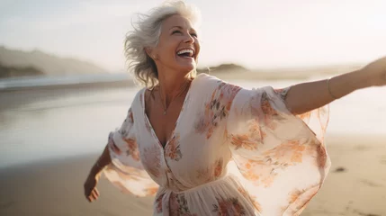  Candid shot of a glimmering, joyful, and optimistic senior woman, smiling and celebrating life on the beach at sunset with a floral dress by the ocean. © Sintrax