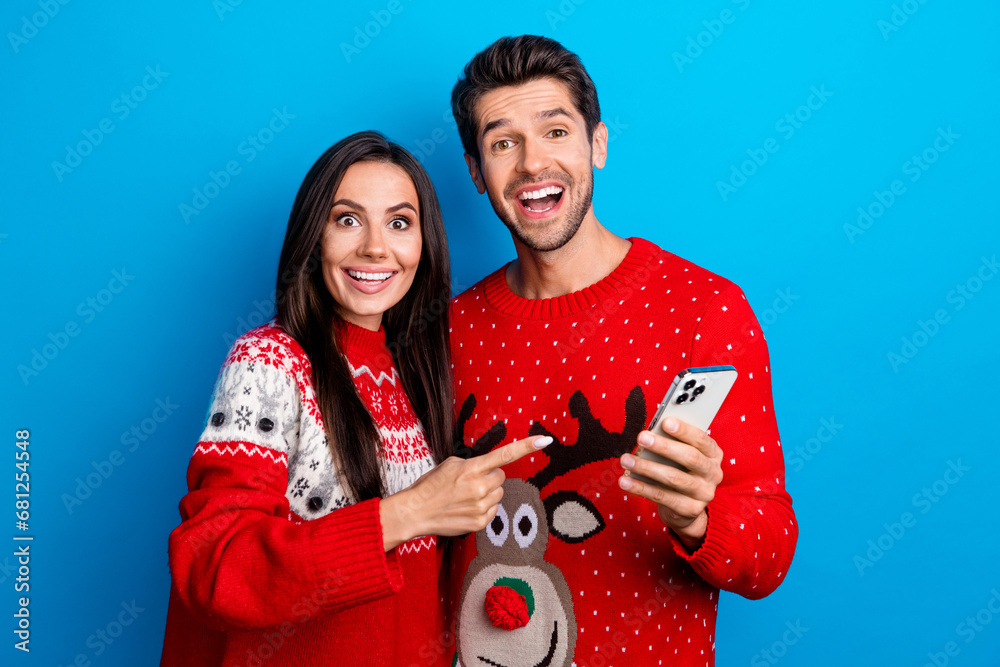 Poster Photo portrait of pretty young lovers excited point telephone wear x-mas ornament red sweaters isolated on blue color background