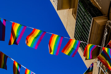 small rainbow flag against the sky in a Spanish city - obrazy, fototapety, plakaty