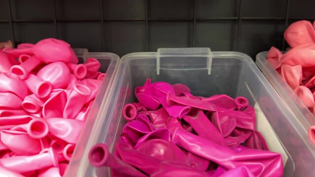 Many pink balloons deflated in a plastic box on a shelf in a store for holiday events and celebrations. Uninflated balloons in the gift shop.