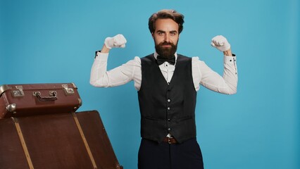 Modern bellboy flexing muscles in studio, showing off strength underneath his formal uniform...