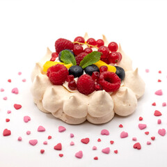 Meringue pavlova dessert, decorated with whipped cream,  berries and mango. Surrounded with heart shaped sprinkles. Photographed against a white background.