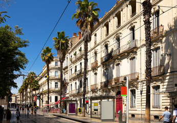 Fototapeta na wymiar View of vibrant cobbled street with tram tracks, typical architecture and tall palm trees in French city of Montpellier on sunny summer day .
